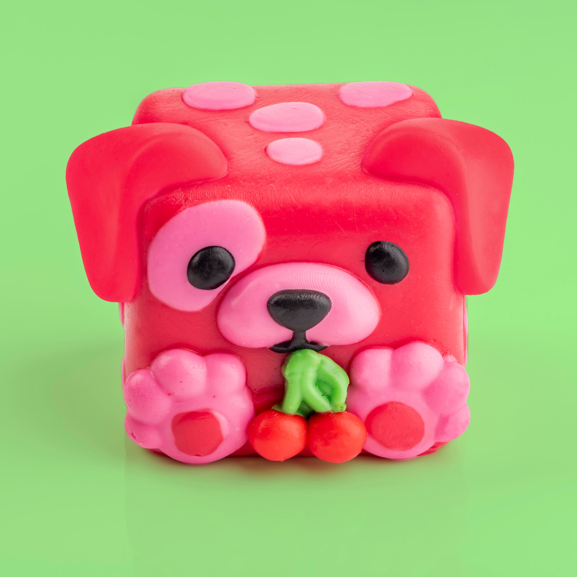 Shirley the dog Mushykinz taba squishy top front view on a green background holding red cherries