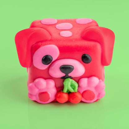 Shirley the dog Mushykinz taba squishy top front view on a green background holding red cherries