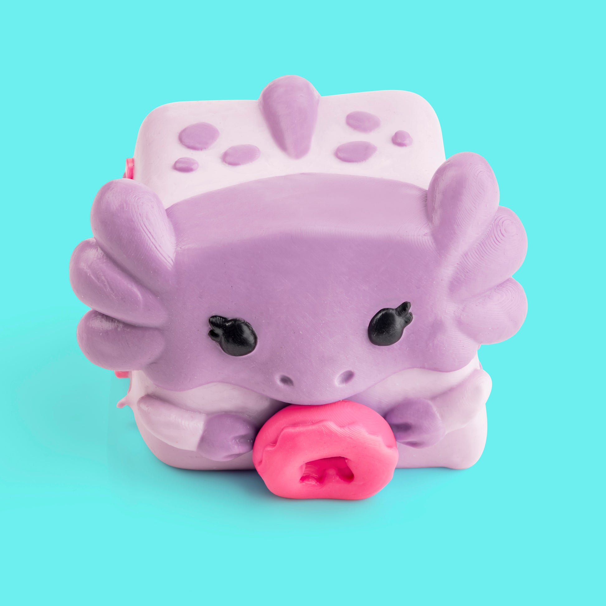 Mochi the Axolotl Mushykinz taba squishy top front view on a teal background holding a pink donut