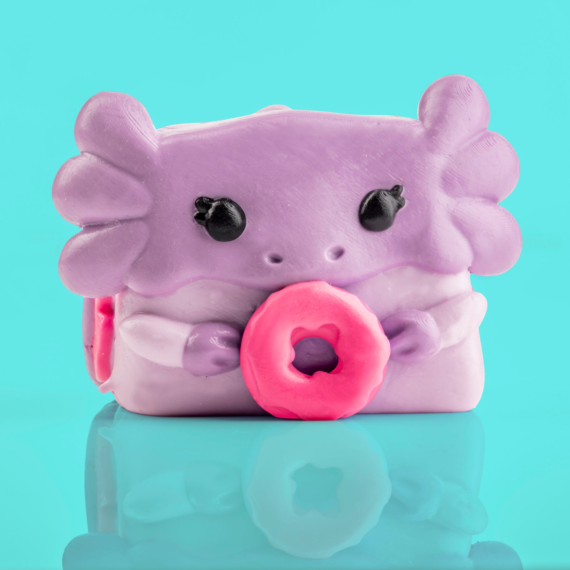 Mochi the Axolotl Mushykinz taba squishy front view on a teal background holding a pink donut