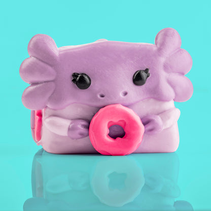 Mochi the Axolotl Mushykinz taba squishy front view on a teal background holding a pink donut